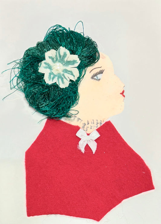 Handmade portrait of a woman in profile. She has dark green textured hair with a light green flower and pearl in the centre. She wears a red outfit with a small white bow.