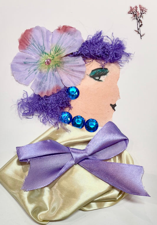 A woman has dark purple hair with a light purple flower as an accessory. She wears a gold blouse with a light purple bow placed in the center. She has sapphire blue gem earrings and a necklace. A dainty flower sits in the top right corner of the card.