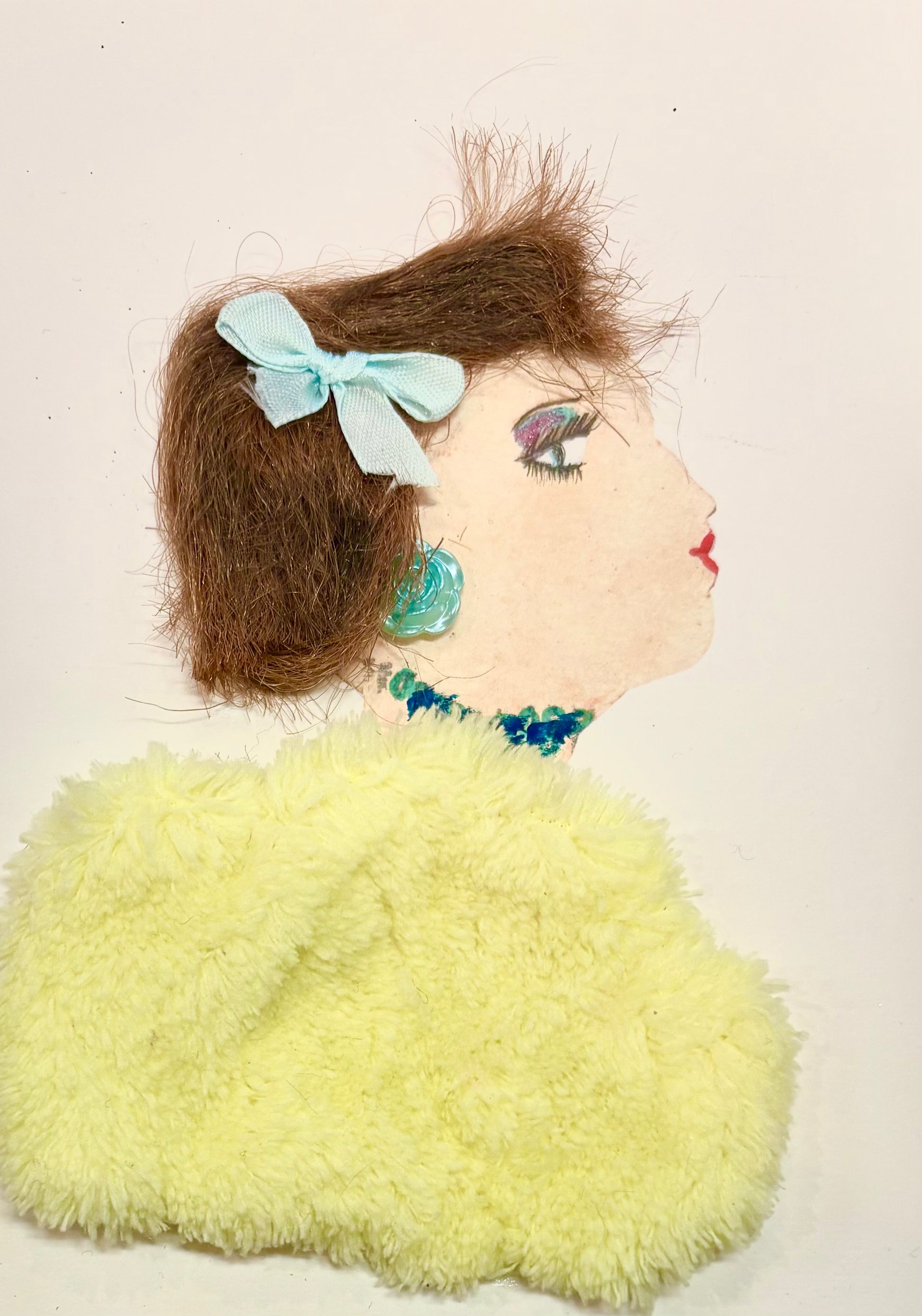 A woman with brown hair wears a mint green bow in her hair. She has a pale fuzzy yellow blouse and a turquoise rose earring and necklace.