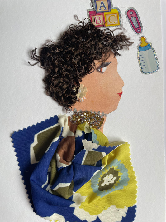 I handmade this card of a woman named Lambeth Lucy. She’s shown in profile with curly brown yarn hair, red lips, and soft makeup. Her gold-toned earring and glittering neckline add sparkle to her look. She wears a vibrant floral-patterned fabric in blue, green, yellow, and cream. Around her are baby-themed stickers, ABC blocks, a bottle, and a dummy clip, suggesting a nurturing, playful spirit.