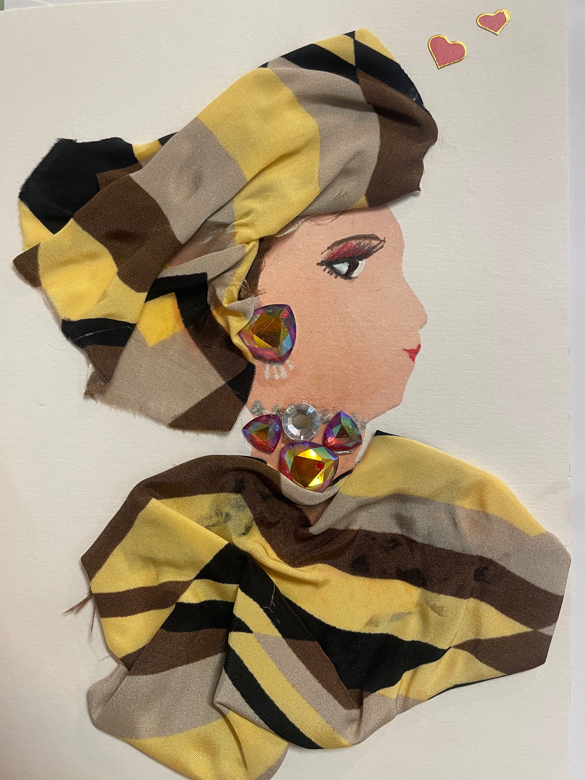 This is a handmade card of a woman named Leyla Ludgate. She wears a striped turban and matching fabric wrap in tones of yellow, brown, and black, with bold gem earrings and neckline decorations. Two heart stickers are in the background.