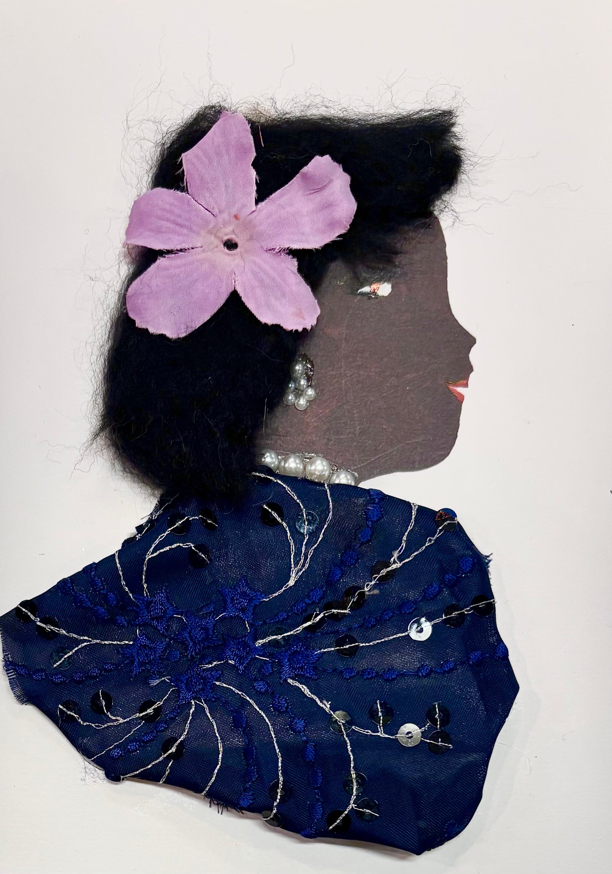 In this picture shows a woman wearing a purple flower in her hair. She has black hair and wears a dark blue top with a bit of sprarkel. This picture is shows a black worman . its is a tactle card