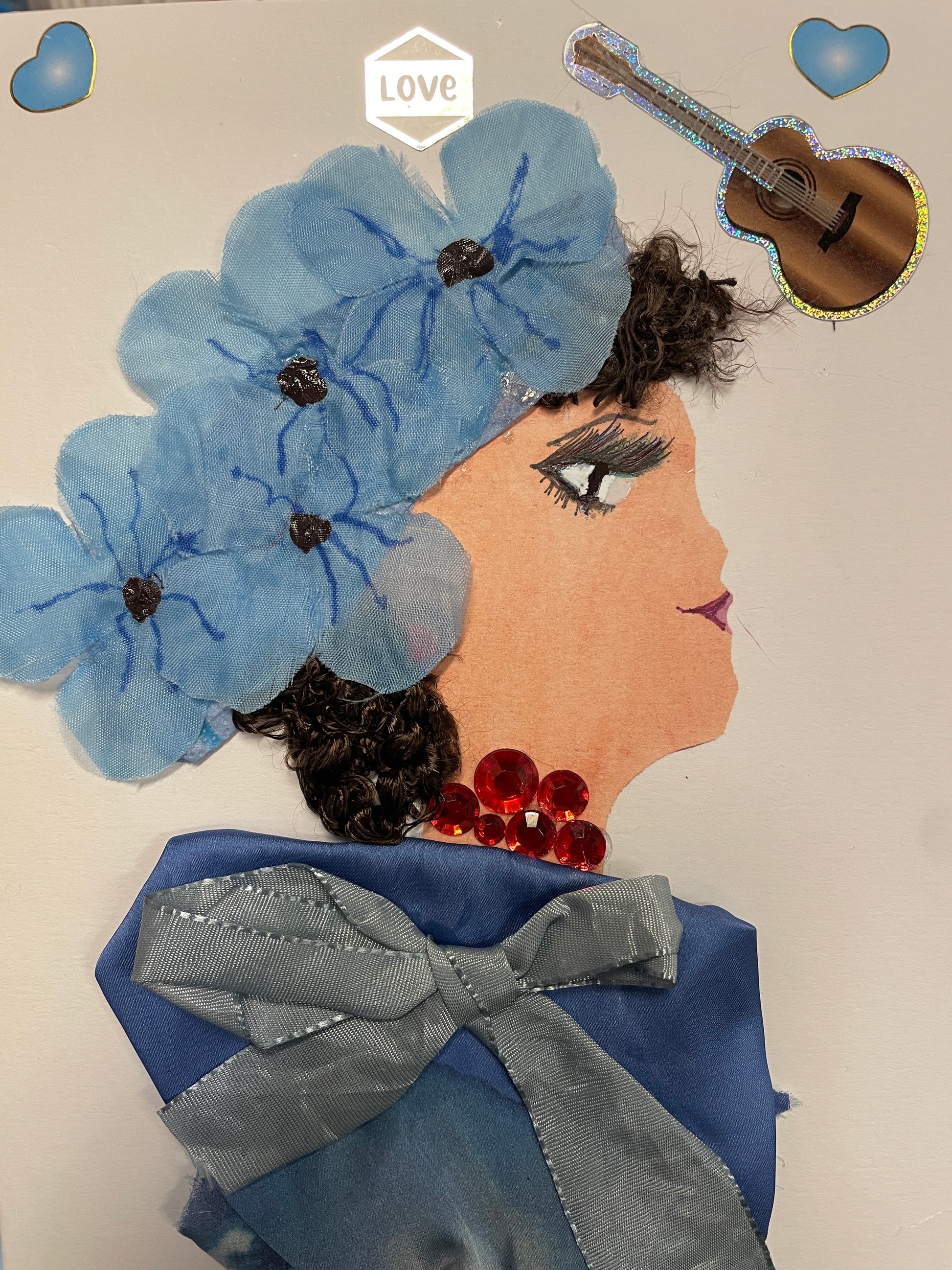 Handmade card of a woman with curly hair, blue floral headwrap, red gemstone necklace, and a blue satin dress with blue bow. A guitar and hearts decorate the background.