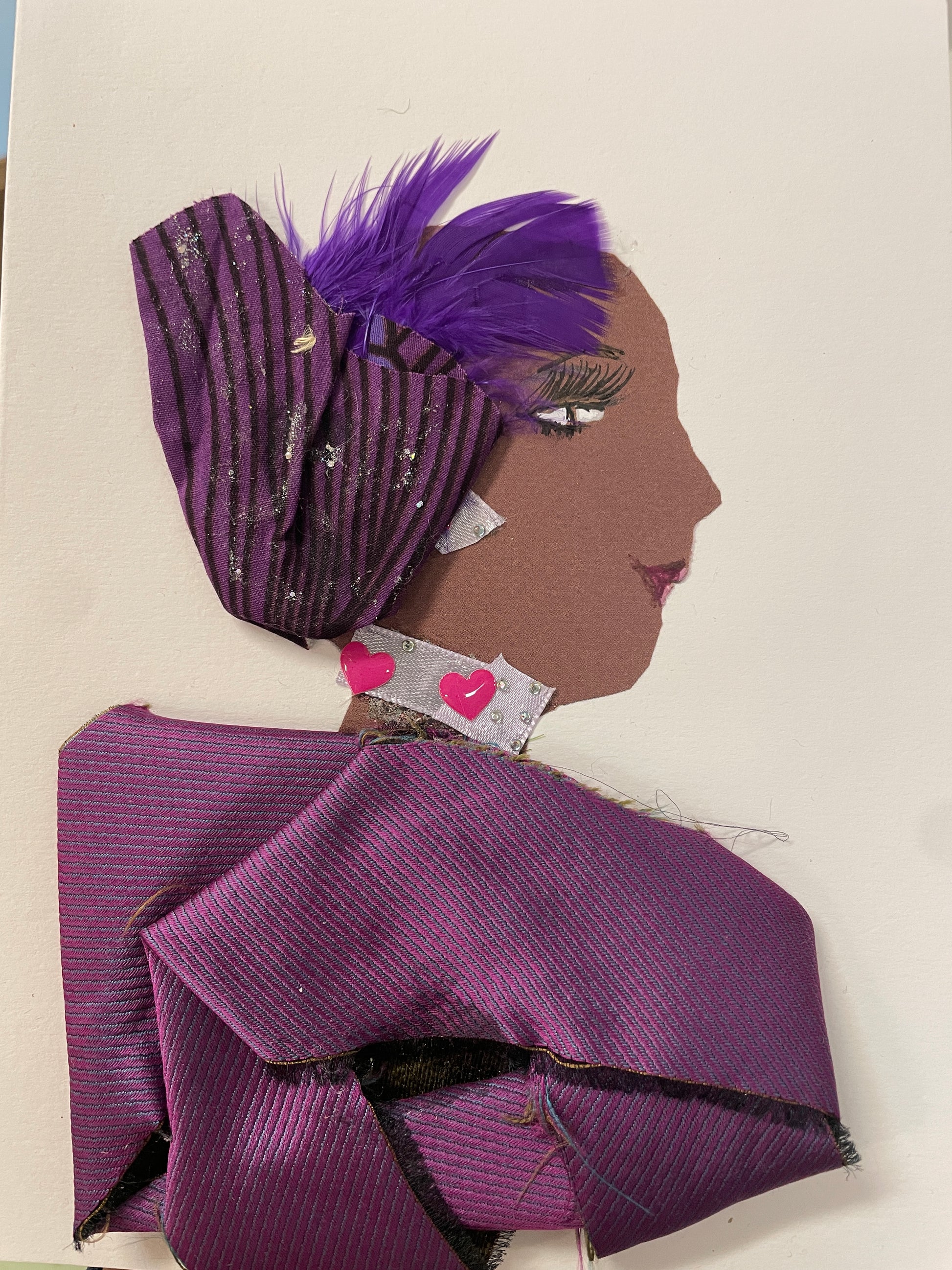 This is a handmade card of a woman named Miraculous Manjula. She wears a purple feathered hat and a structured purple outfit with pink hearts near the collar.