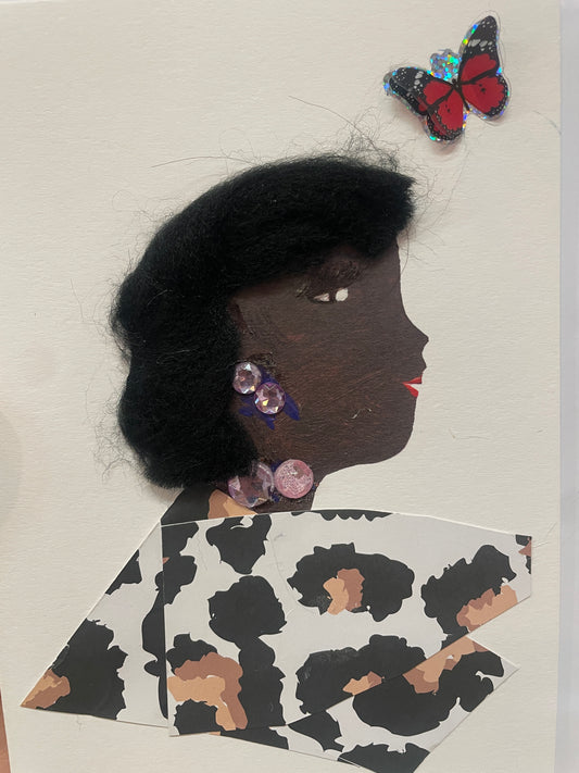 This is a handmade card of a woman named Mohak with black wool hair, purple earrings and necklace, and a cow-print outfit. A shiny butterfly sticker is nearby.