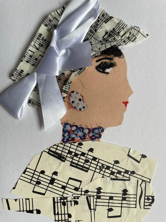 I handmade this card of a woman named Musical Melody. She’s shown in profile with dramatic lashes, red lips, and a textured black updo. Her headwrap and outfit are made from printed sheet music, and a large white satin bow is tied elegantly across the top. She wears a patterned earring and a hand-painted necklace with layered blue and pink dots, adding playful charm to her graceful look.
