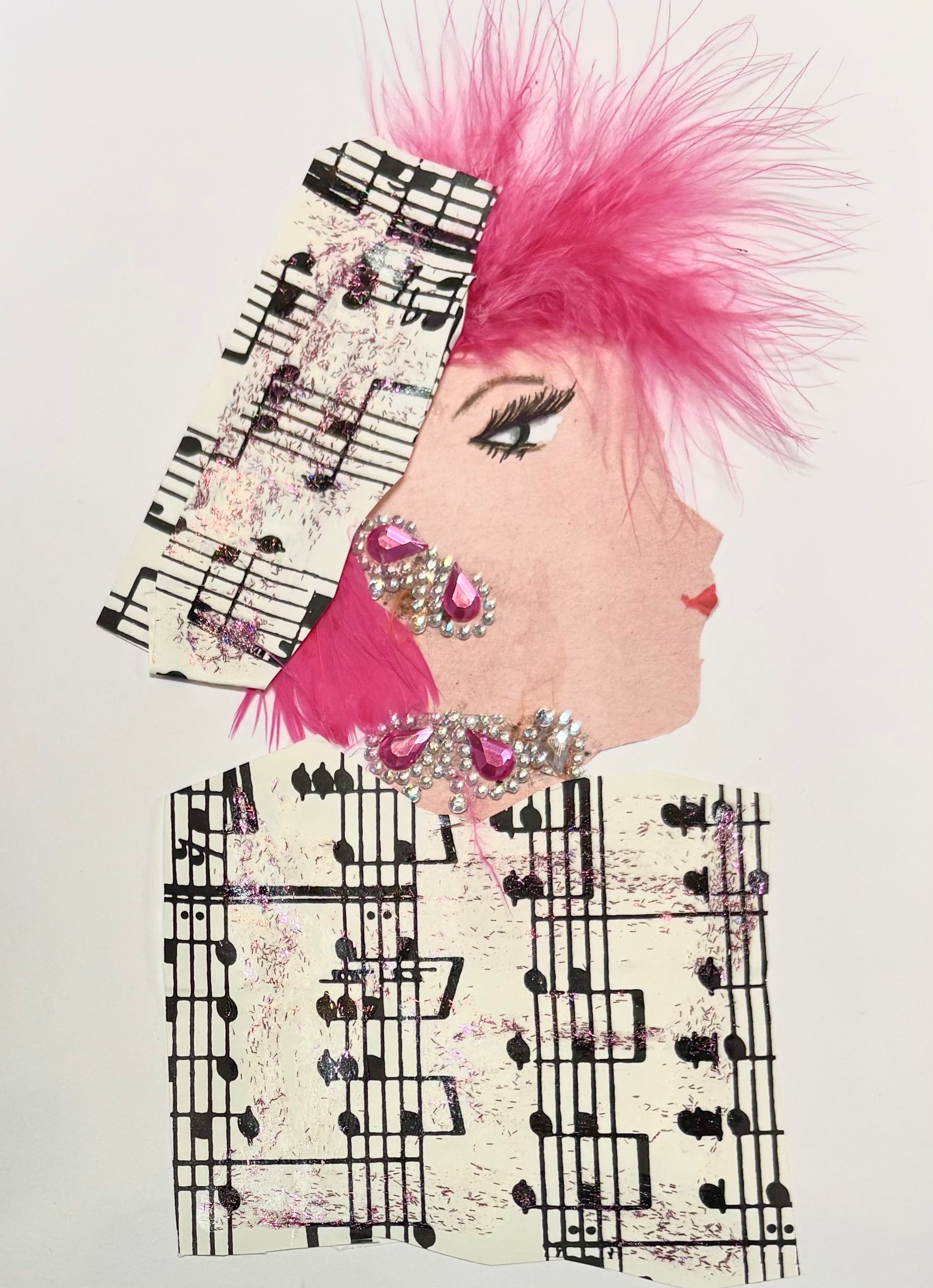 I handmade this card of a woman named Musical Margaret. She’s shown in profile with striking lashes, red lips, and a vibrant plume of pink feathers in her hair. Her headwrap and outfit are made from distressed sheet music paper brushed with hints of glittery pink. She wears dramatic pink and silver gem earrings and a matching embellishment at her neckline, adding sparkle to her theatrical style.