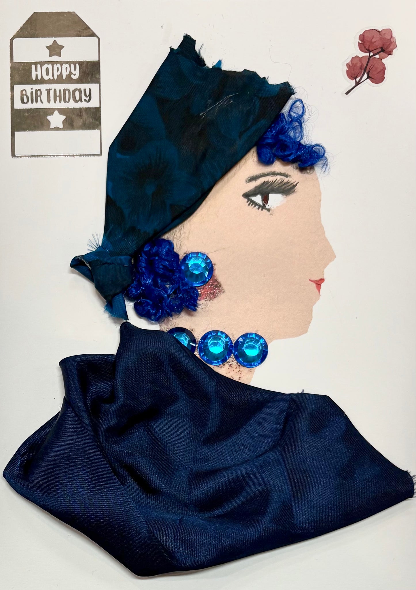 A woman has a deep blue headwrap with her curly blue hair peaking out. She has a dark blue blouse and wears blue gem earrings and a necklace. There is a "Happy Birthday" sticker in the top left and a dainty flower in the top right.