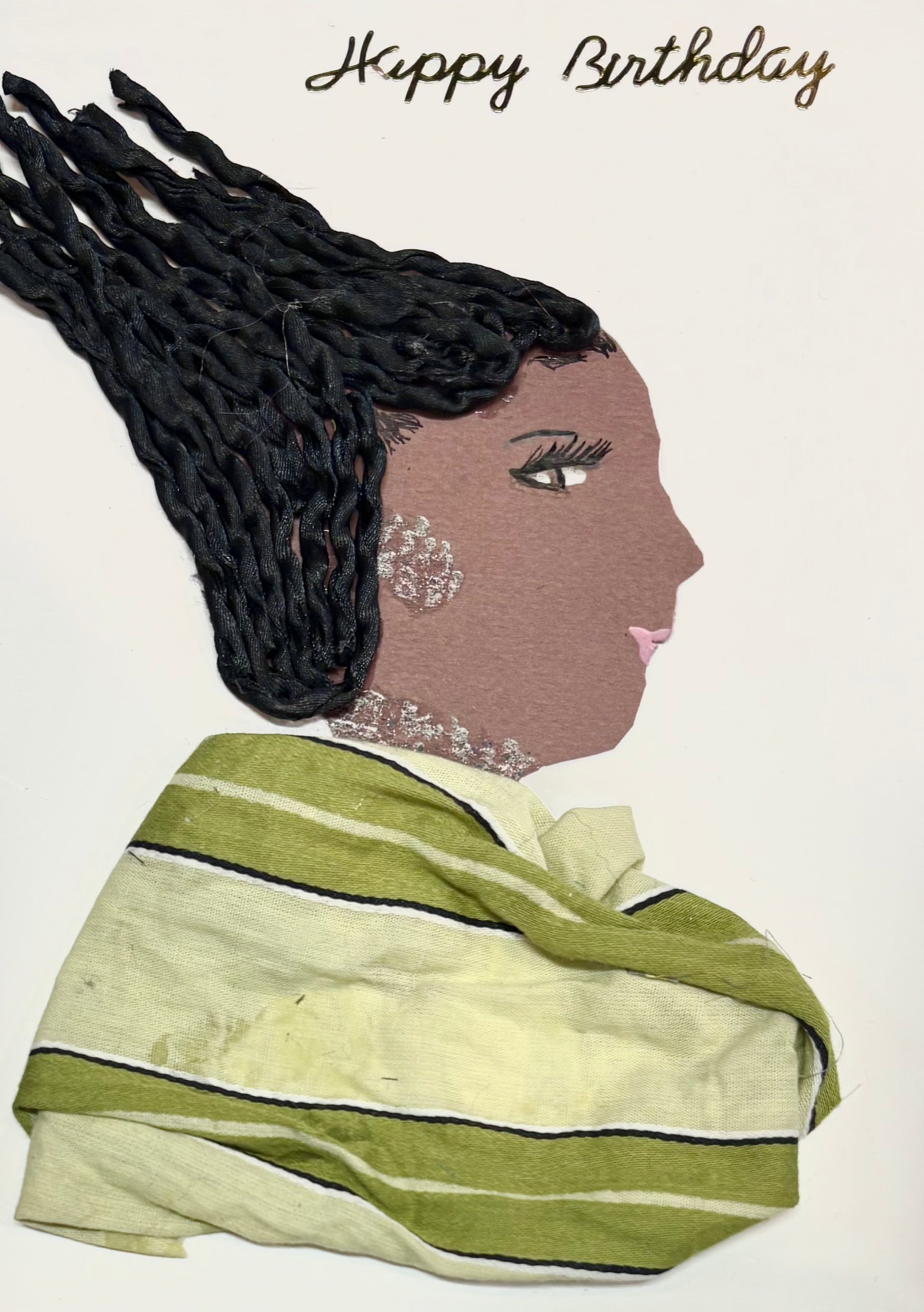 A woman has a braided hairstyle with a monochrome green blouse with green stripes. She has a silver earring and necklace. Happy Birthday is spelt in golden letters in the top right of the card.