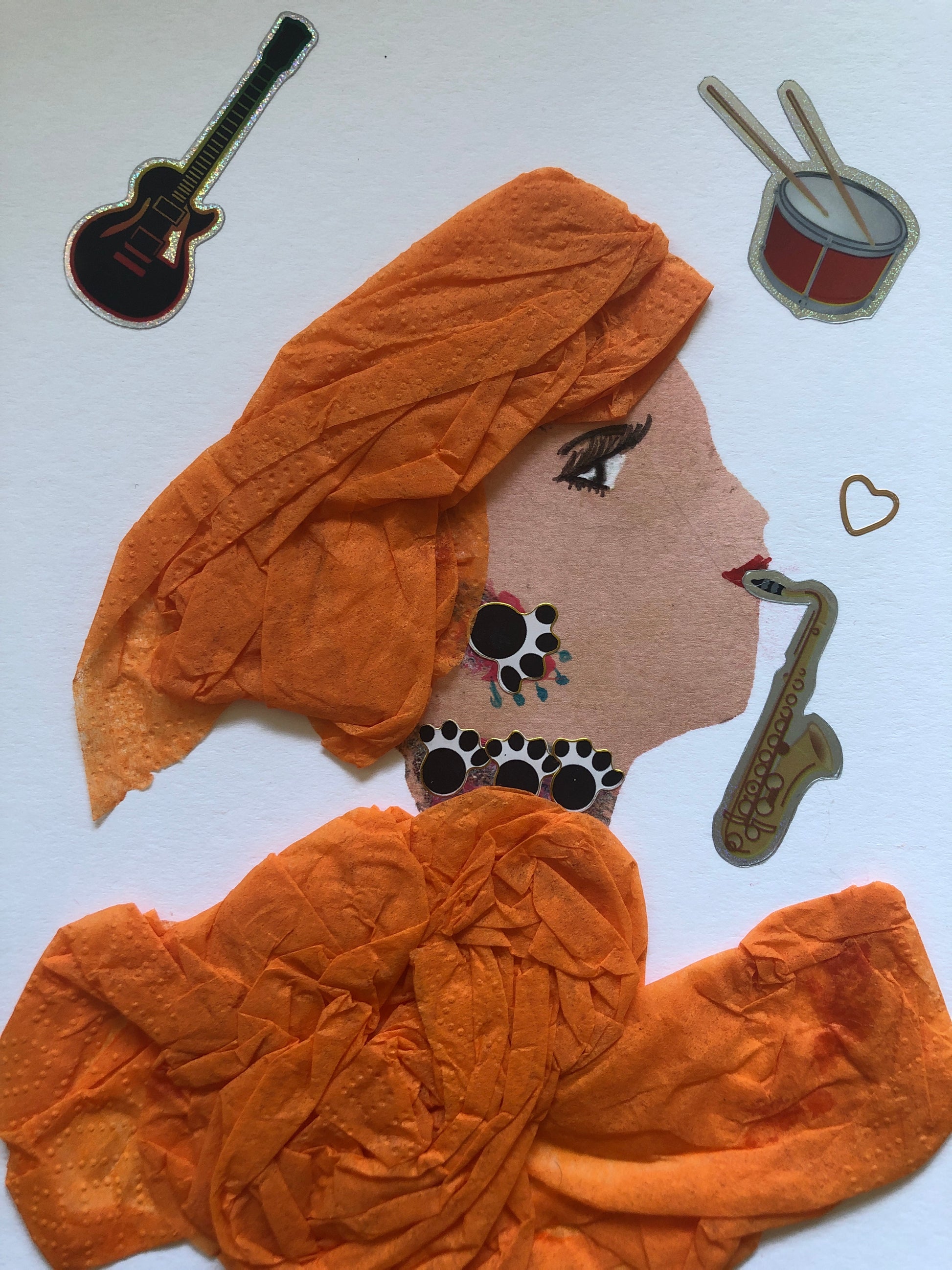 I handmade this card of a woman named Orange SAXOPHONE. She’s shown in profile with expressive eyes, red lips, and layered orange fabric wrapping her hair and outfit. Her bold black-and-white jewellery is accented with small teal dots. A gold saxophone sticker appears by her mouth as if she’s playing, with a floating heart nearby. Around her are playful stickers of a guitar and drum, adding to her lively, musical vibe.