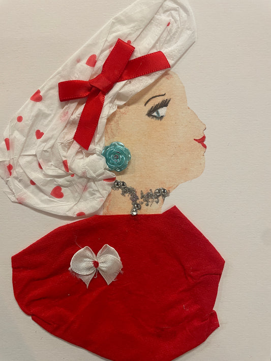 This is a handmade card of a woman named Paige Paddington. She wears a white head wrap with red hearts, a red bow, a blue rose earring, and a red top with a small white bow.
