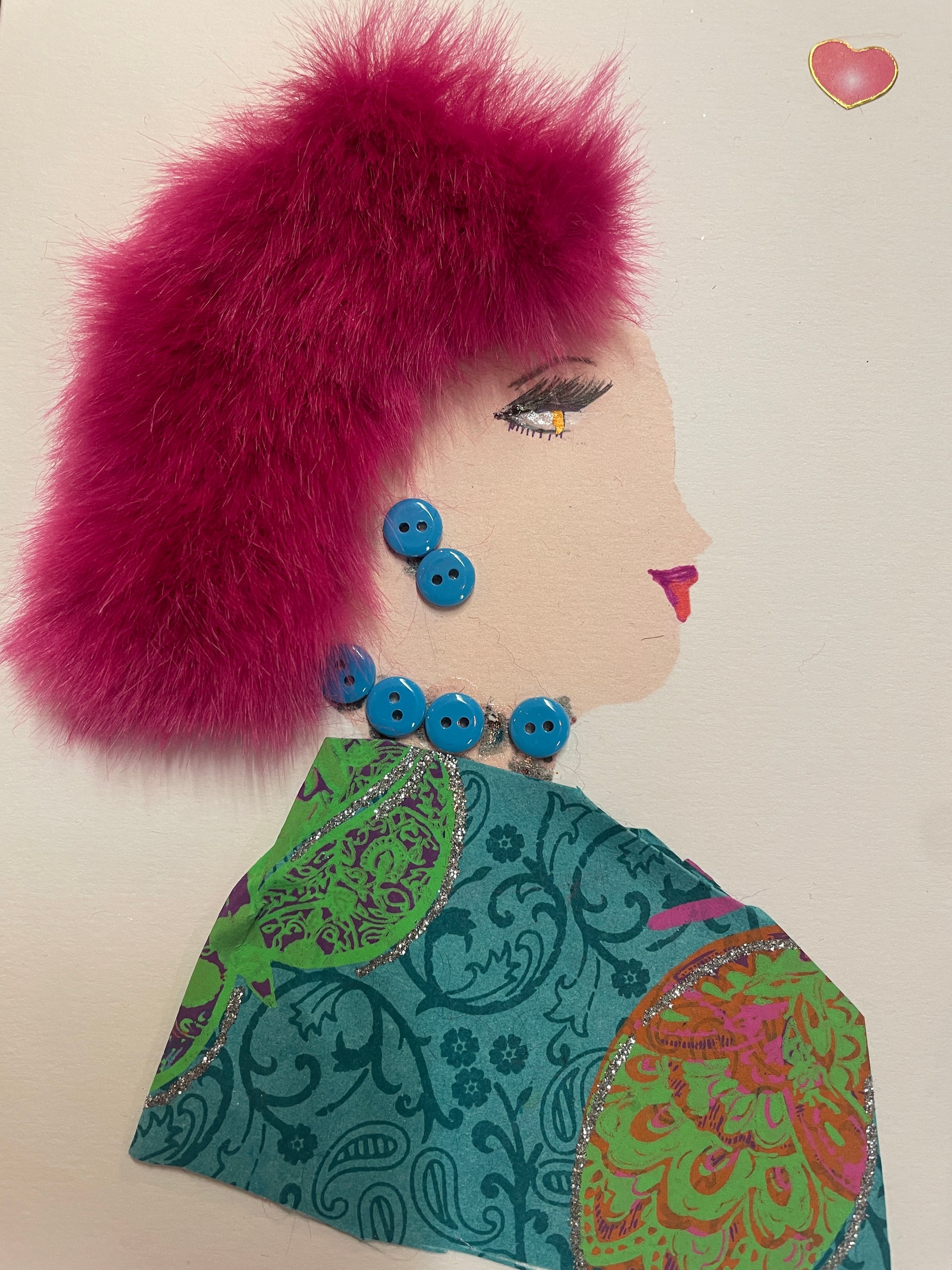 A handmade card of a woman with fluffy magenta hair, a blue button earring and necklace, and a bright teal patterned outfit. A pink heart sticker floats above her.