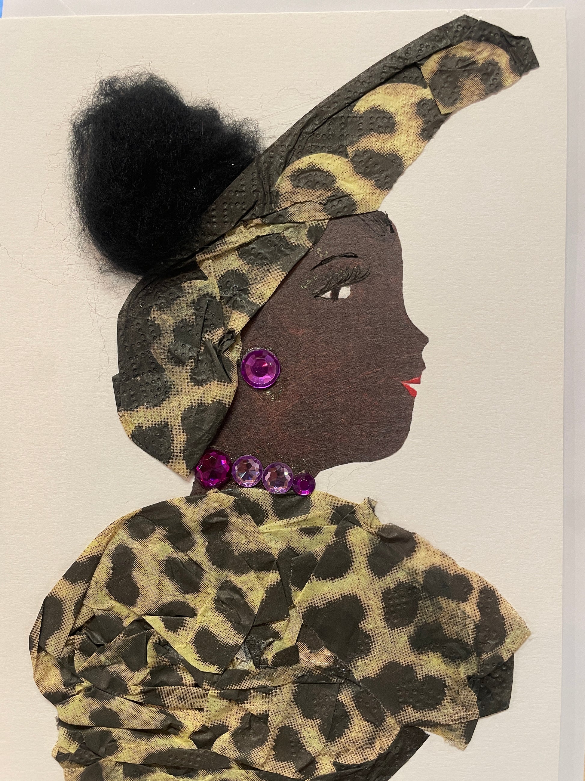 This is a handmade card of a woman named Primrose Paddington. She is dressed in golden leopard-print fabric with a matching high turban and a round black hair bun. Her jewellery features purple gem earrings and a matching necklace.
