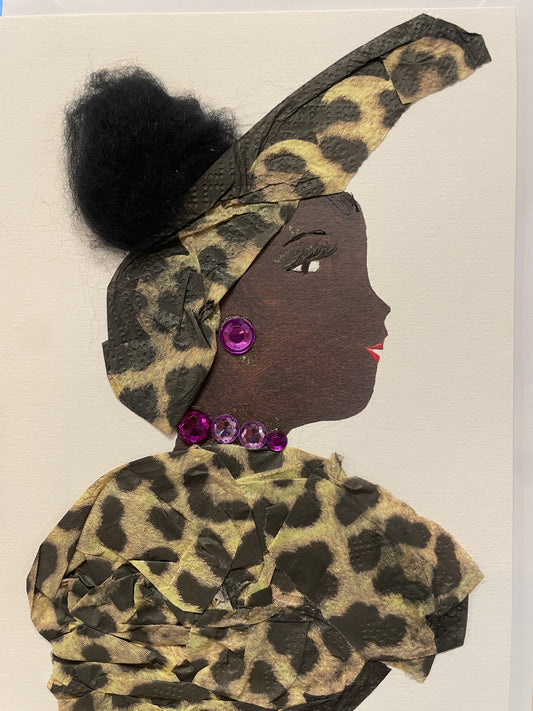 This is a handmade card of a woman named Primrose Paddington. She is dressed in golden leopard-print fabric with a matching high turban and a round black hair bun. Her jewellery features purple gem earrings and a matching necklace.