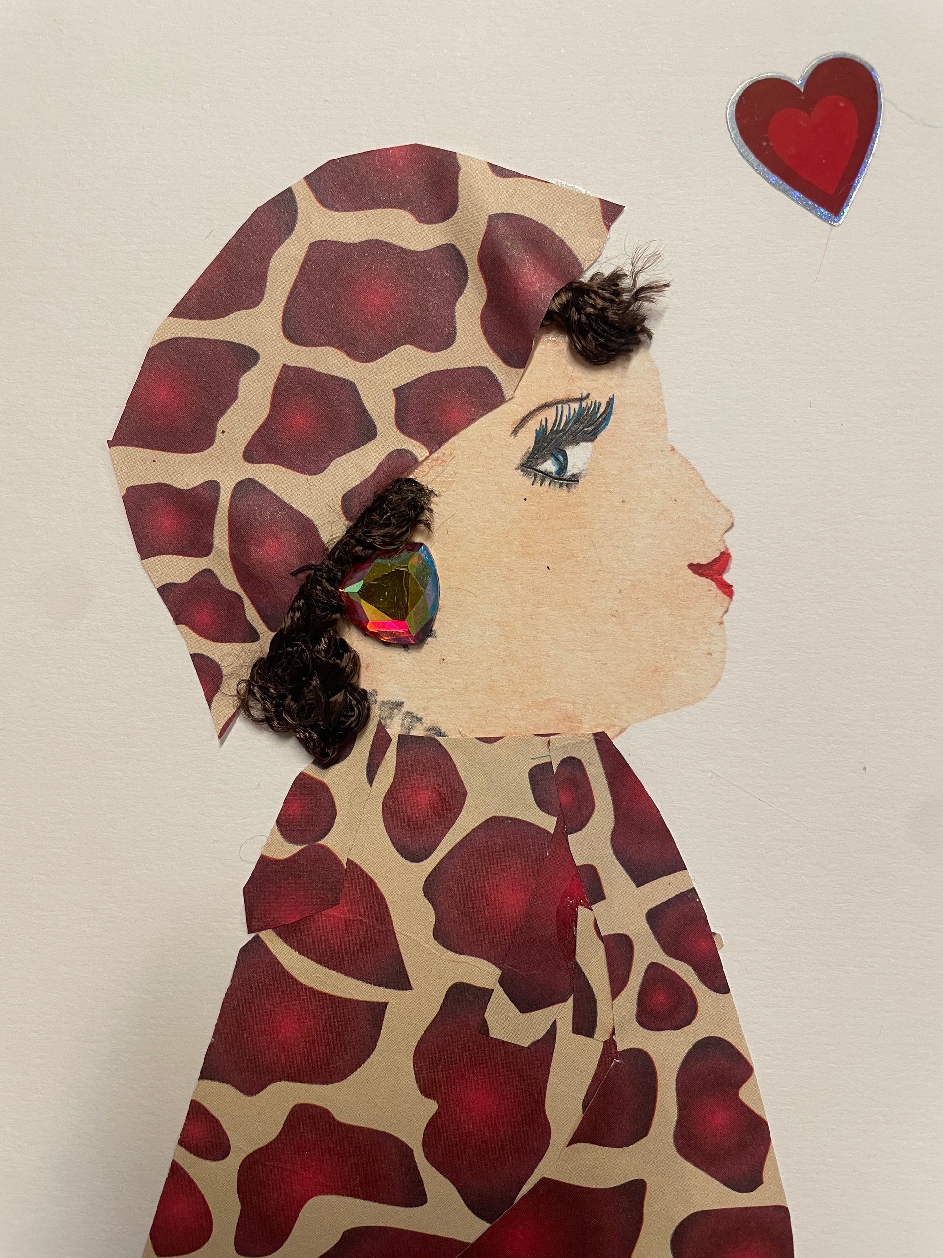 Handmade card of a woman in a full red-and-tan giraffe-print outfit with matching headwrap. She has curly dark hair, large multicolor gem earrings, and a red heart sticker above her head.