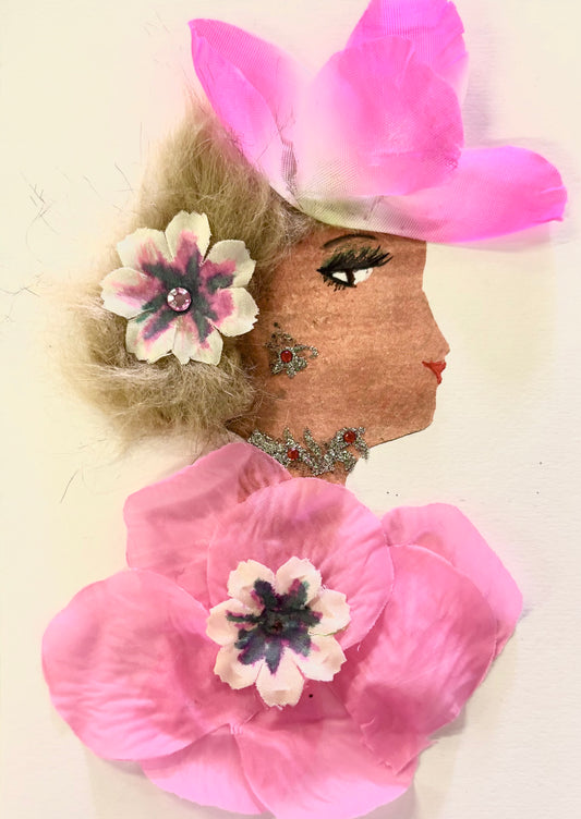 Handmade portrait of a woman in profile. She has light brown curly hair with a pink and white flower in it, and wears a large pink flower hat. Her dress is made from pink fabric flowers, and she has glittery red and silver decorations on her face and neck.