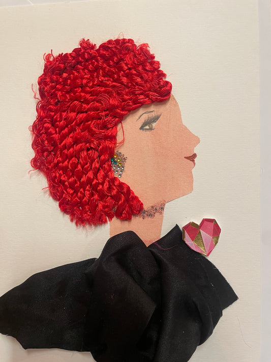 A handmade card of a woman in profile with bright red textured hair, a multi-coloured gem earring, and a black outfit with a pink and gold patterned heart near her shoulder.