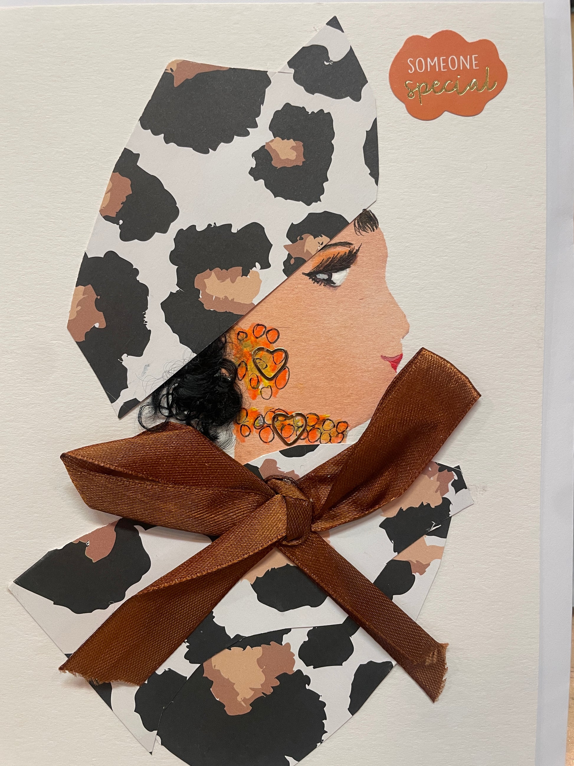 Handmade art card of a woman in side profile, wearing a cream and black printed head wrap and matching outfit with a large brown satin bow. Her earrings and necklace are made of orange beads, and the top right corner includes a sticker that says “Someone Special.”