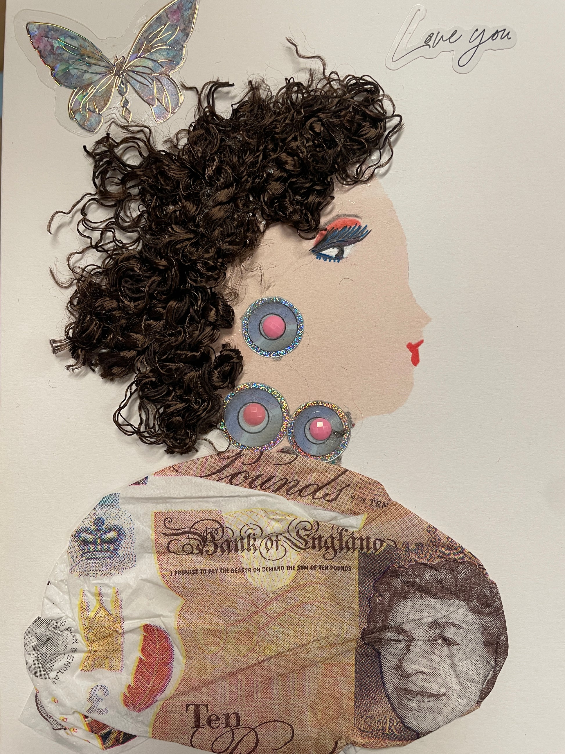 Handmade card of a woman with curly brown hair, large round earrings with pink gems in the center, and a dress made from printed ten-pound notes. A butterfly and “Love you” sticker float above.