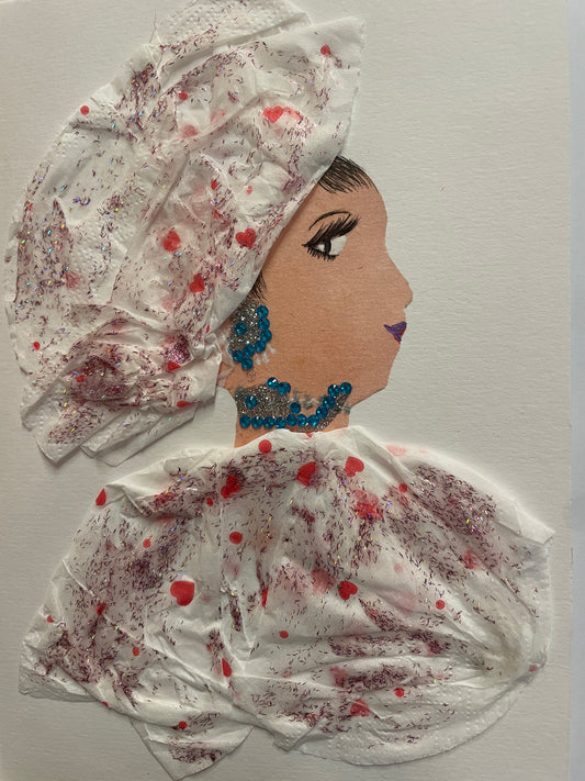 A handmade card showing a woman in profile wearing a white outfit with pink glitter and hearts. She has bright blue earrings and a necklace, and a head wrap made from matching white material.