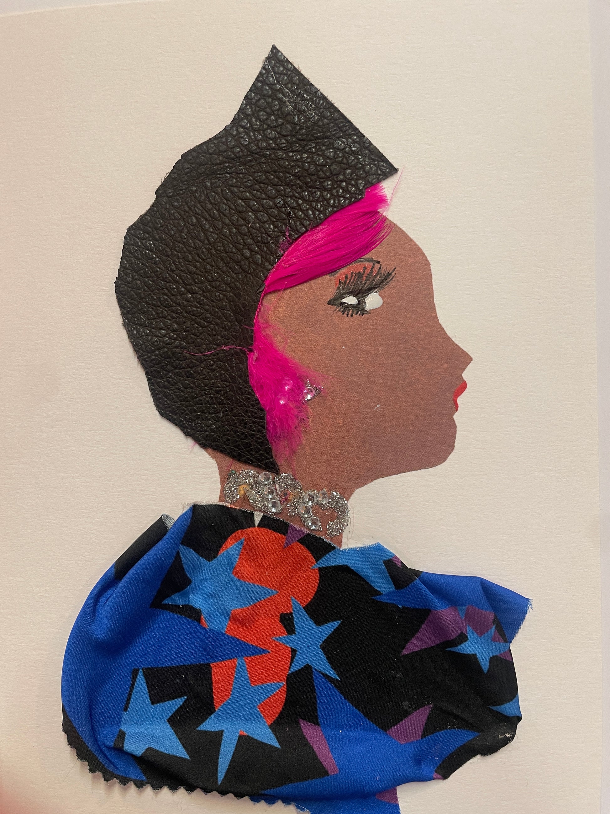 A handmade card featuring a woman in profile with a black hat and visible streaks of bright pink hair. She wears a sparkly silver necklace and a deep blue outfit with colourful stars.