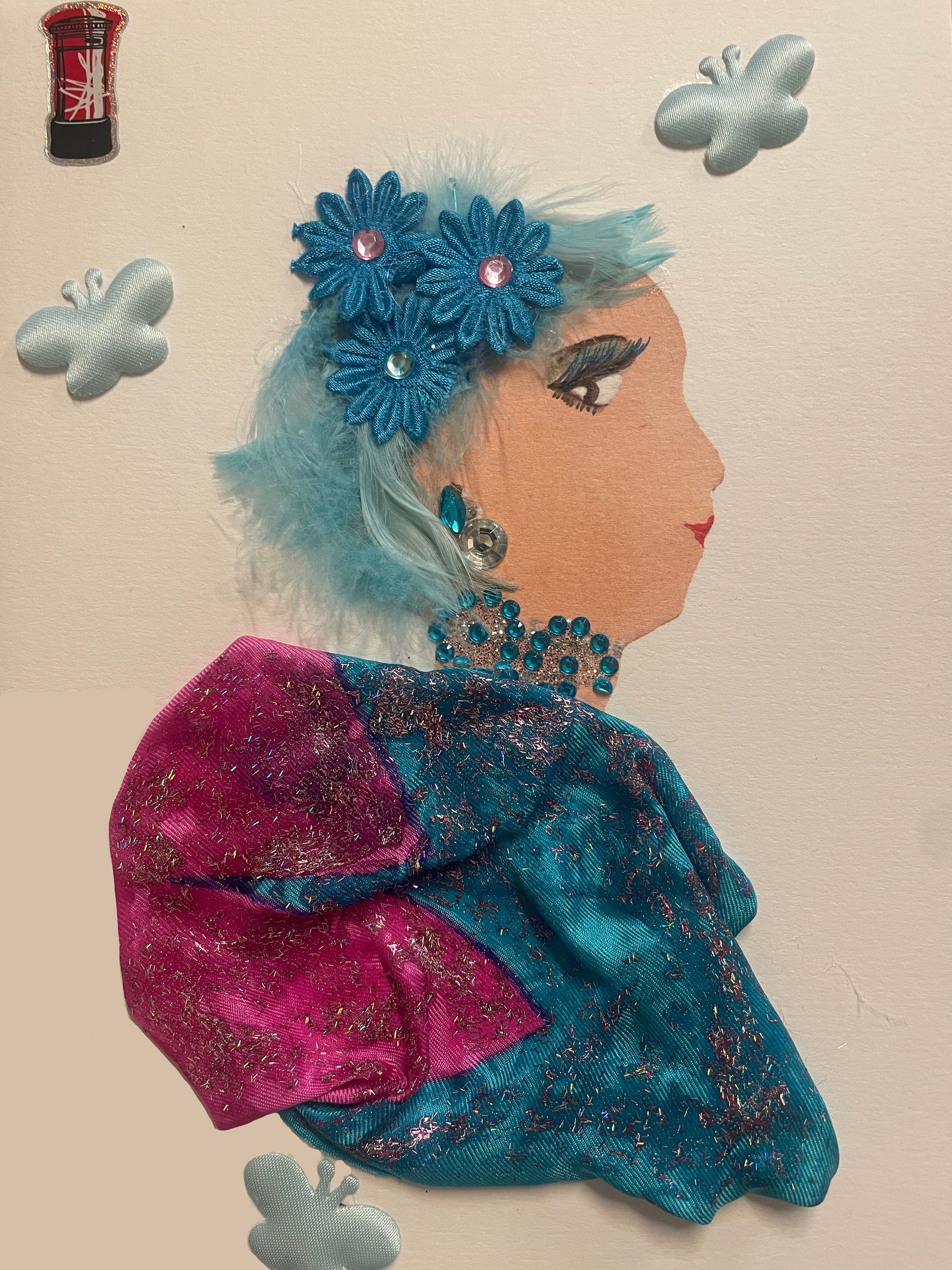 This is a handmade card of a woman named Tierna Tower. She has pastel blue fuzzy hair with teal flowers, wears sparkly blue jewellery and a bright blue-and-pink dress. Stickers include a red telephone box and multiple butterflies.