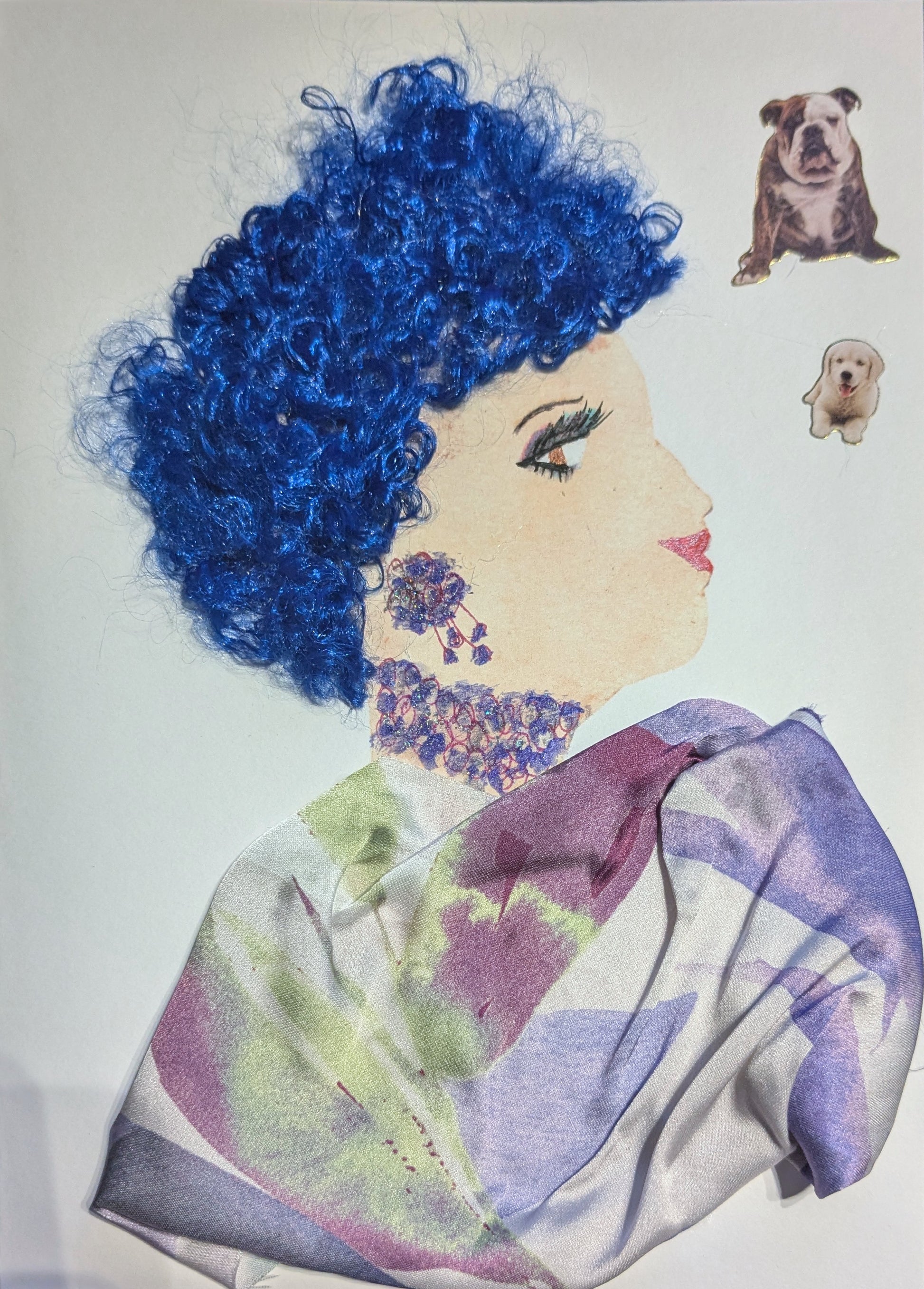 I handmade this card of a woman named Violet Bellflower. She’s shown in profile with bold eye makeup, pink lips, and vivid curly blue yarn hair. Her jewellery is drawn in purple and pink with floral detailing, and she wears a flowing scarf made from pastel fabric in lavender, green, and burgundy. Two small dog stickers, a bulldog and a puppy, float beside her on the right.