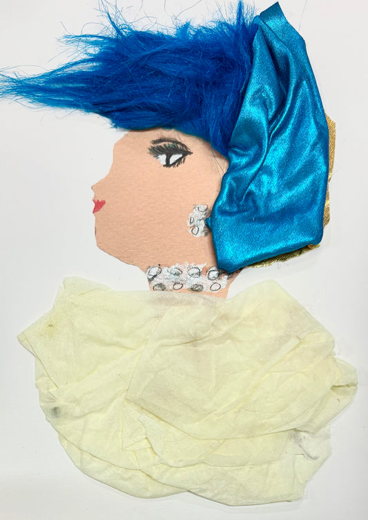 I handmade this card of a woman named Wanda Wimbledon. She has bright blue feathery hair with a shimmering blue head wrap. She’s wearing silver dot earrings and a matching necklace, paired with a soft cream-colored dress made from textured fabric.