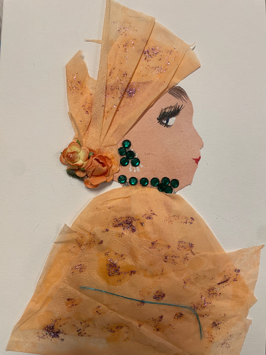 **Wembley Winnie**
A handmade card showing a woman in a soft orange outfit with sparkles. She has a matching headwrap with glitter and orange paper roses. Her necklace and earrings are made of green gems. Her makeup includes long lashes and red lipstick.
