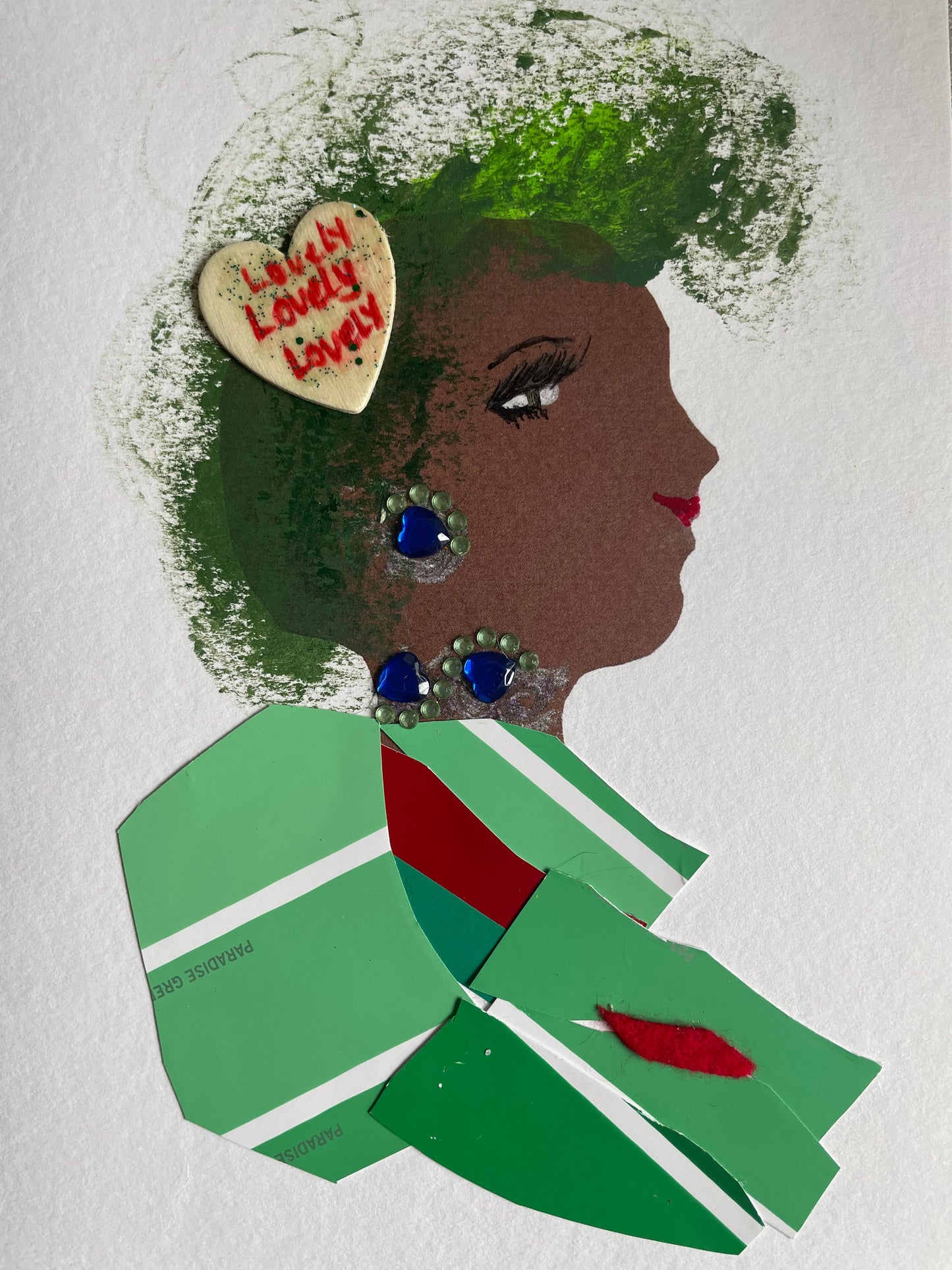 This card depicts a woman with green hair and a white heart that says ‘lovely’ pinned in her hair. She wears a green blouse with red and white stripes. She also wears blue and green jewellery.
