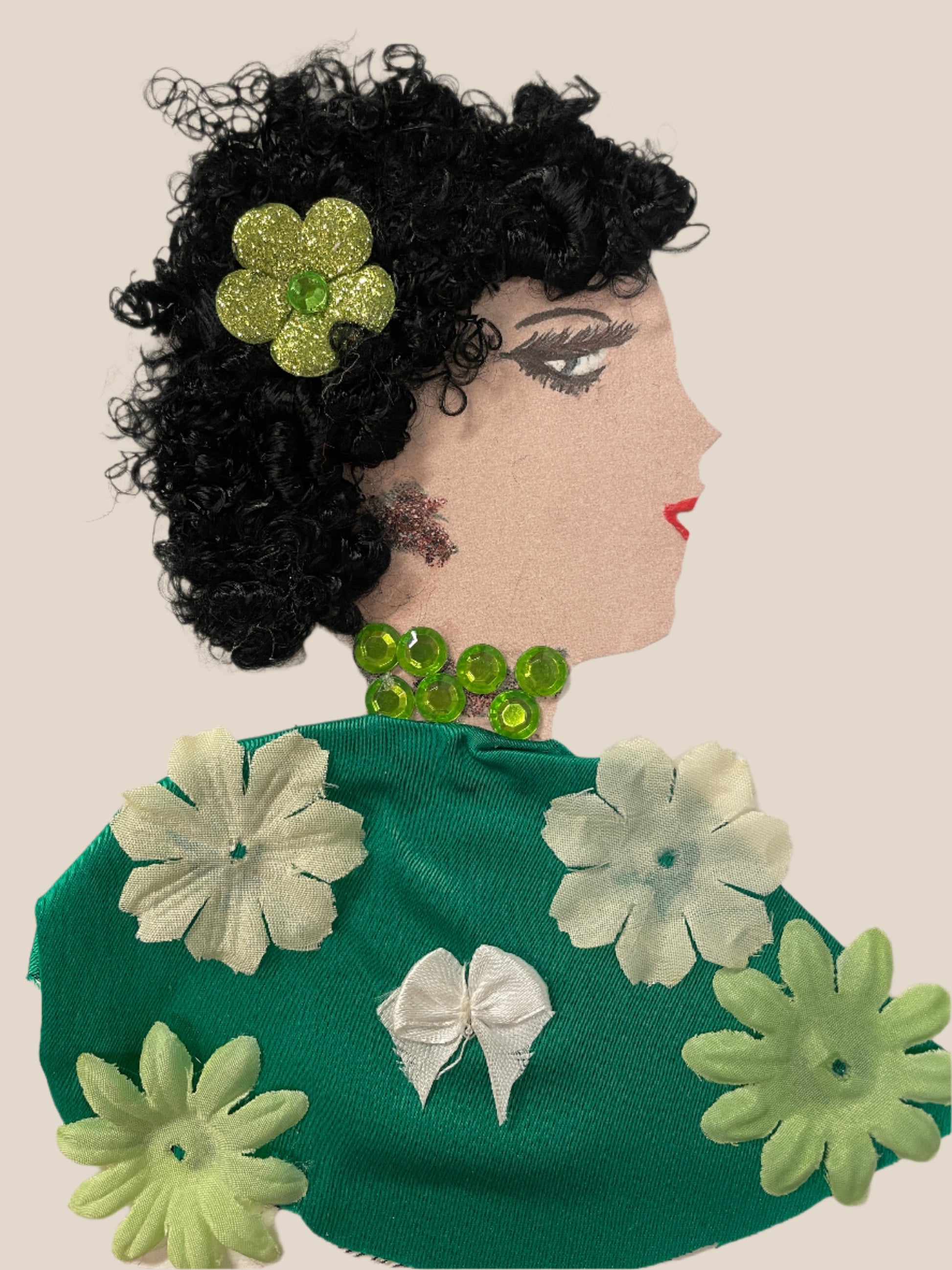 This is a handmade card of a woman named Zariah Greenleaf with curly black hair, a sparkly green flower, and a green dress decorated with soft fabric flowers and a white bow.