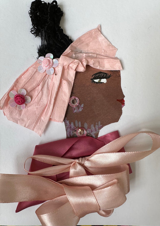 I designed this handmade card of a black woman dressed in a blouse that is composed of two light pink bows. Her hatinator is a light pink, bow-like shape with two flowers, and she has gemstones has jewellery.