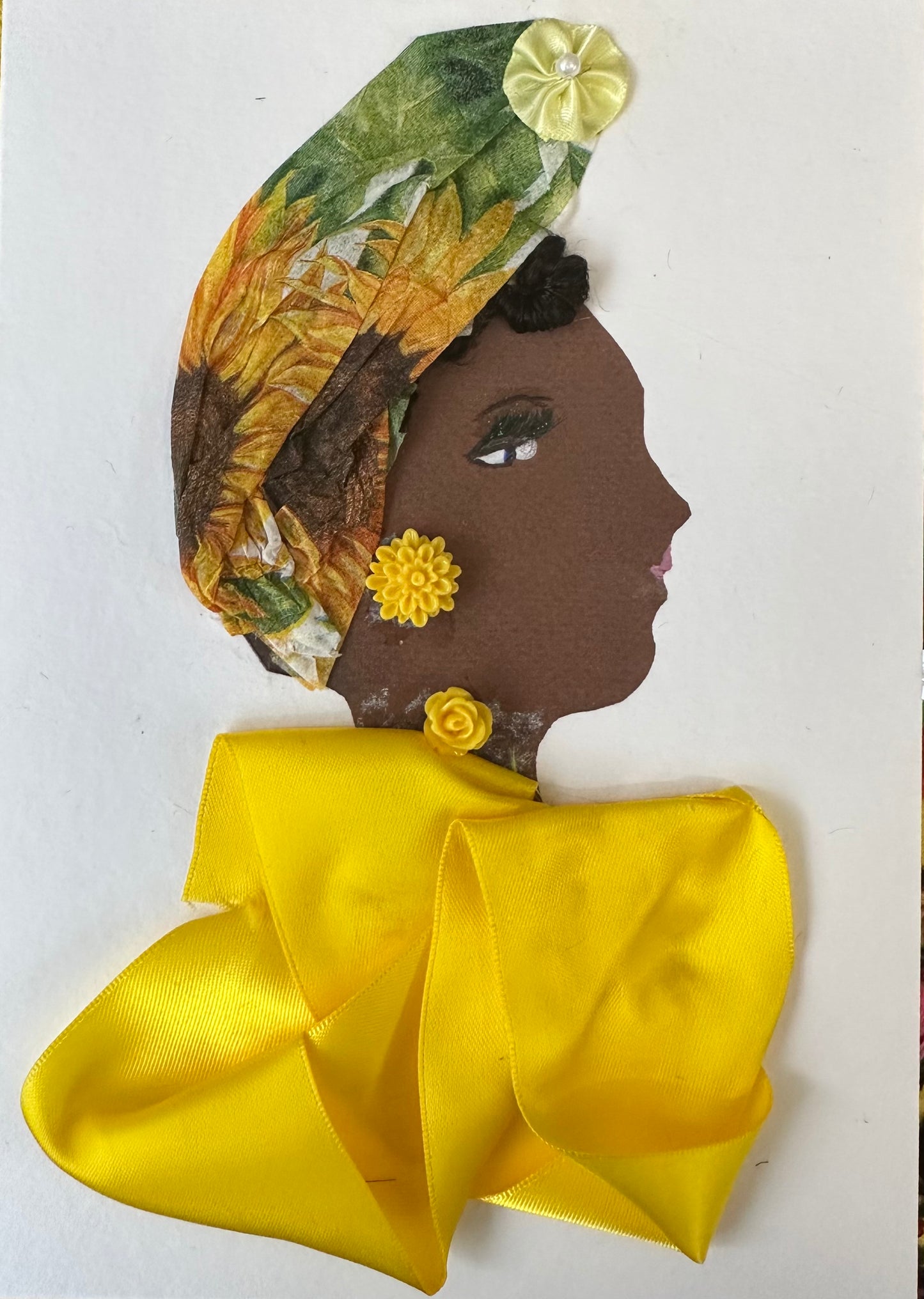I designed this handmade card of a woman wearing a yellow silk-like blouse. Her hatinator is made of a tissue-textured material that is patterned with sunflowers and its leaves. On the top of the hat is a yellow silk-like flower, which matches the bright yellow flower.