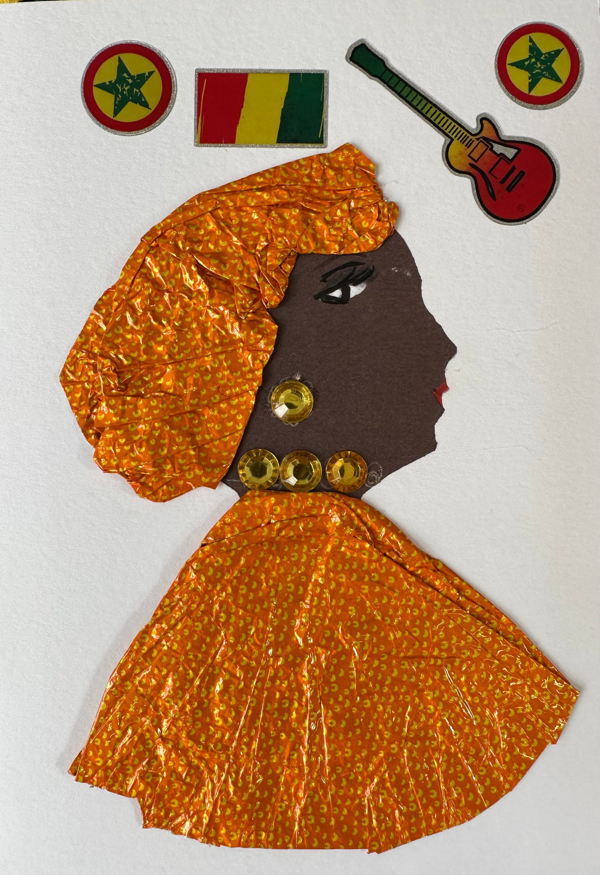 I created this handmade card of Kilburn Kristine. She is dressed in a matching hair wrap and blouse which are orange with small yellow spots. Her earring and necklace are a yellow-gold gemstone. The card is completed with a red, yellow, and green guitar, flag, and stars.
