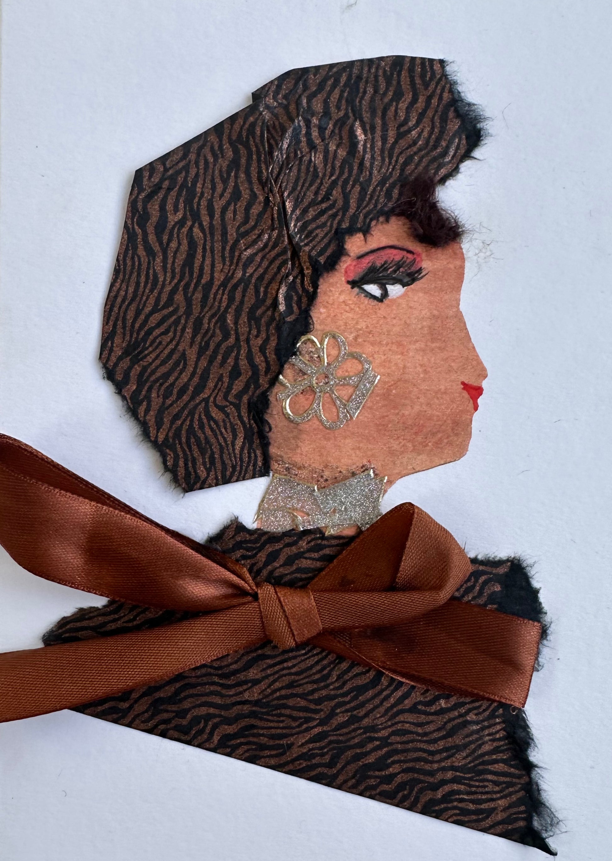 I designed this handmade card of a woman dressed in a brown and black tiger print blouse and hatinator. Her blouse is held together with a chocolate brown ribbon. Her earring is a silver flower which matches her silver necklace.