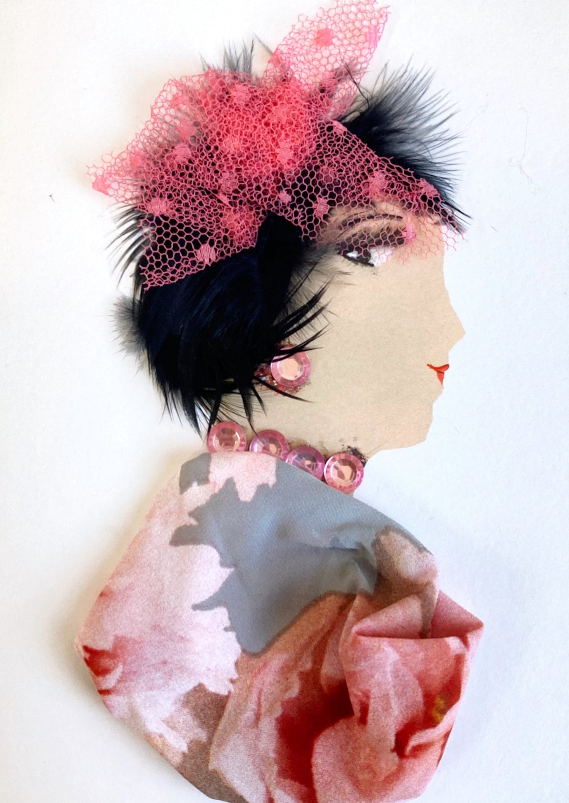 This card has been given the name belinda. She wears a floral blouse which has a grey background and pink roses on it. Her jewellery is made up of pink gems, and she wears a pink netted headpiece in her short black hair.