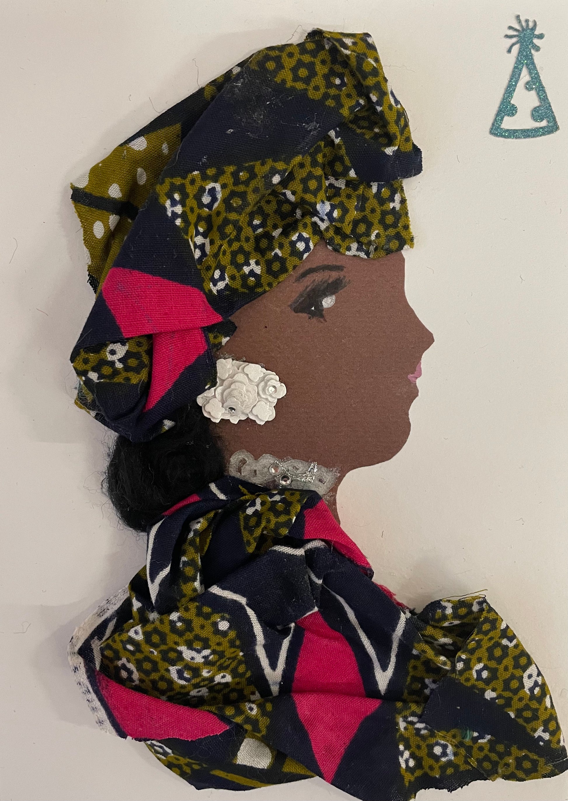 This is a handmade card of a woman named Doctor Clapham. She wears a bold headwrap and matching outfit made from patterned fabric in navy, olive green, white, and bright pink. Her earring is a white floral embellishment, and she has a sparkly silver accessory around her neck. Her face is shown in profile with gentle features and soft pink lips. In the top corner, a small glittery party hat sticker adds a festive touch.