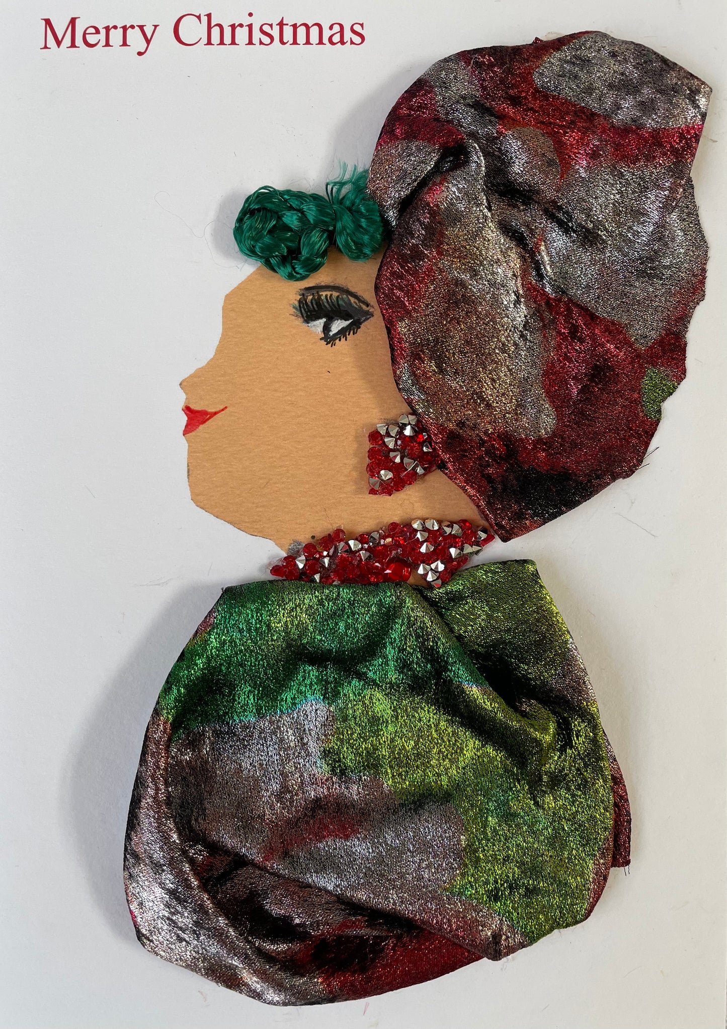 Merry Christmas is written on the top and there is picture of a woman wearing a velvety red and silver hatinator. She has green hair sticking out of the her hatinator. She is wearing sparkly matching red and silver jewellery.  She is wearing a distinctive warm velvety silvery green blouse.This is a unique card which  can be framed as a gift or used as a traditional greeting card. Useful for a birthday or keepsake