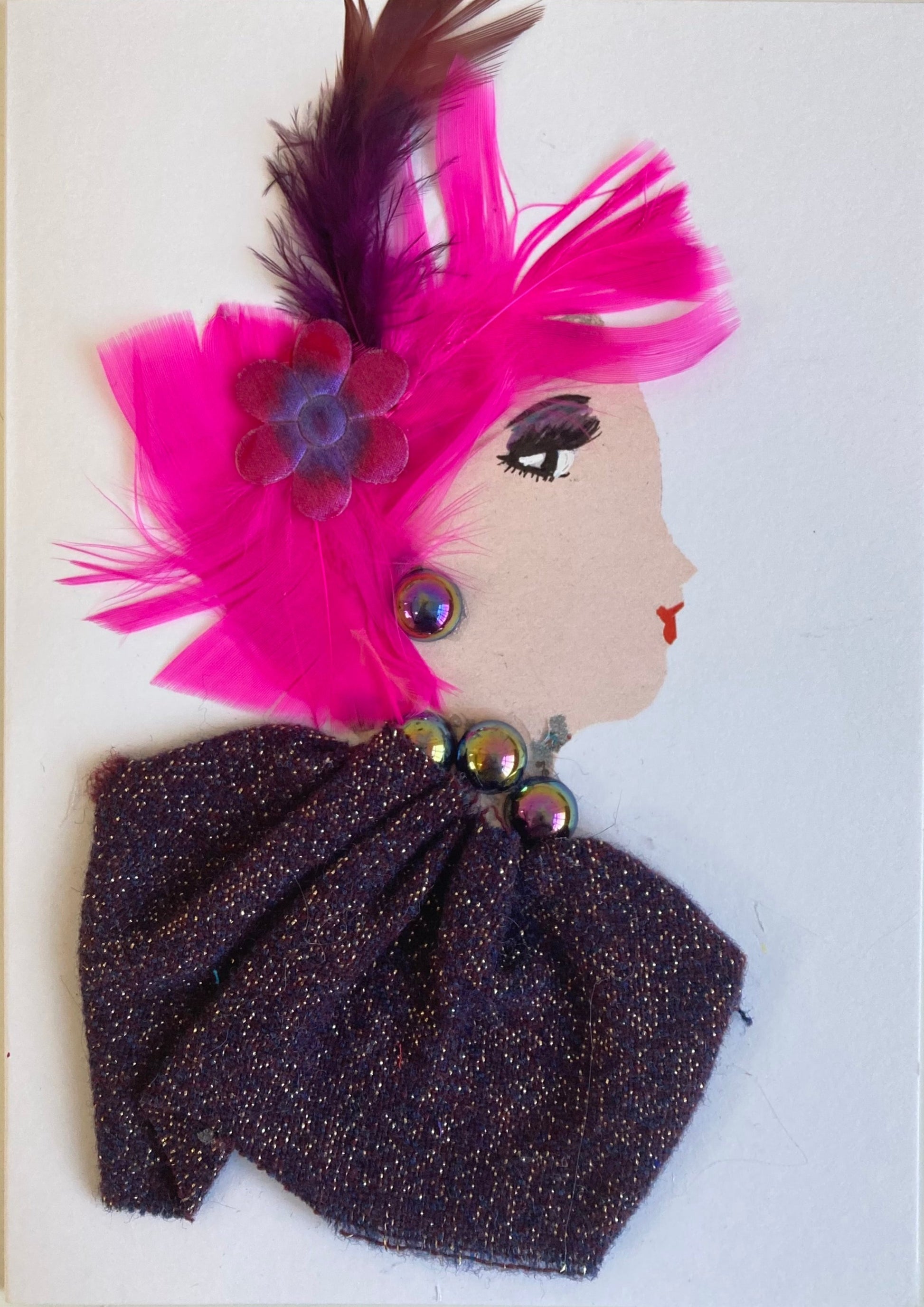 This card is of a woman given the name Regina. Regina wears a blouse made of a recycled purple fabric with gold sparkles in it. Her jewellery is black pearls which have an iridescent shine to them. Her hair is made of electric pink feathers, and she has a small pink flower in it which has a dark purple feather coming out of it.A beautiful card  to frame for your home or the perfect gift for someone to celebrate
