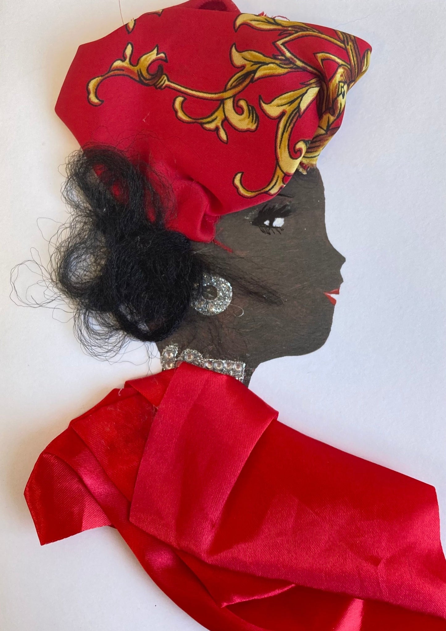 This card has been given the name Tabitha. Tabitha wears a red silk blouse with a silver necklace and earrings. She wears a red headscarf which has a gold print on it, and her black hair can be seen underneath it.