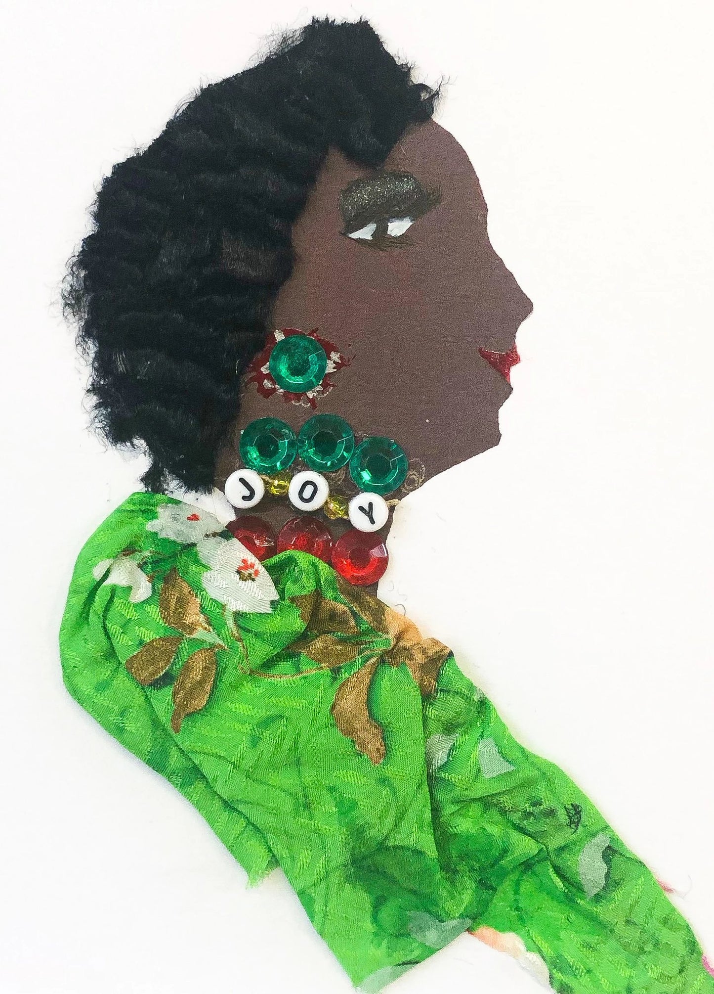 This card has been given the name Jubilee Joy. she wears a green nature patterned blouse. She has three different necklaces, one red gems, one green gems, and one that says joy in beading. She has short black hair, and her green earring is peeking out.