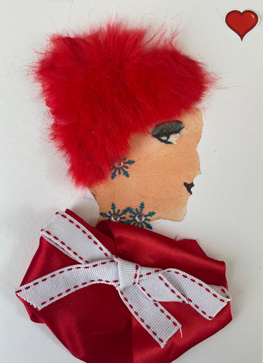 I designed this card of a woman called Victoria Valentine. She is a white woman who is wearing a red blouse with a white ribboned bow with red stitching at the edges. She has red vibrant hair. She has a matching blue diamanté snowflake designed necklace and earrings. There is a red heart in the right corner.