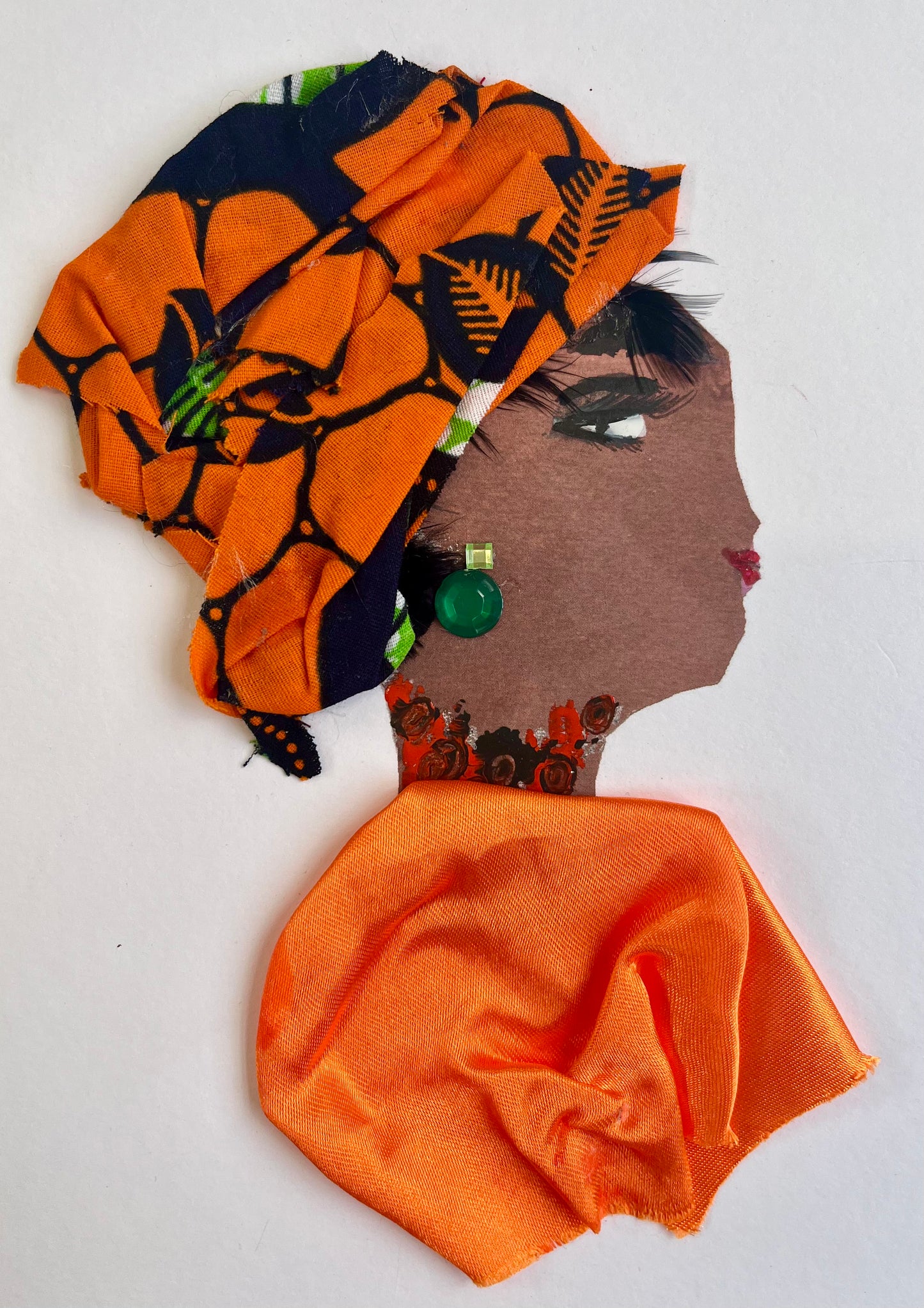 This card is called Kehlani. She wears a bright orange blouse and a headscarf which has orange and black in it. Her earring is a green gemstone.