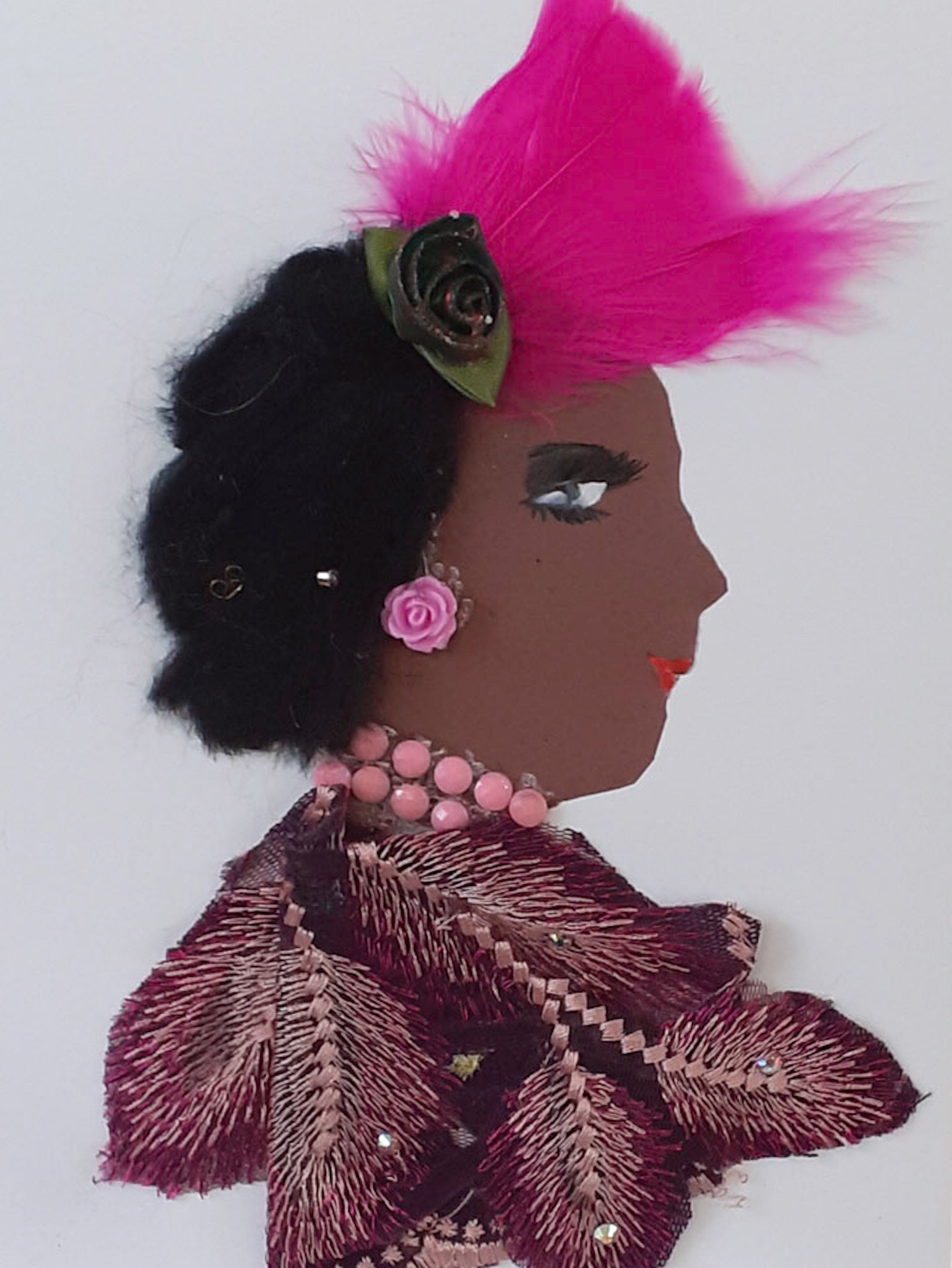 This card is called Dollis. She wears a flowery overlay as a blouse, and a pink feather in her black hair with a small green rose next to it. Her jewellery is pink gems.