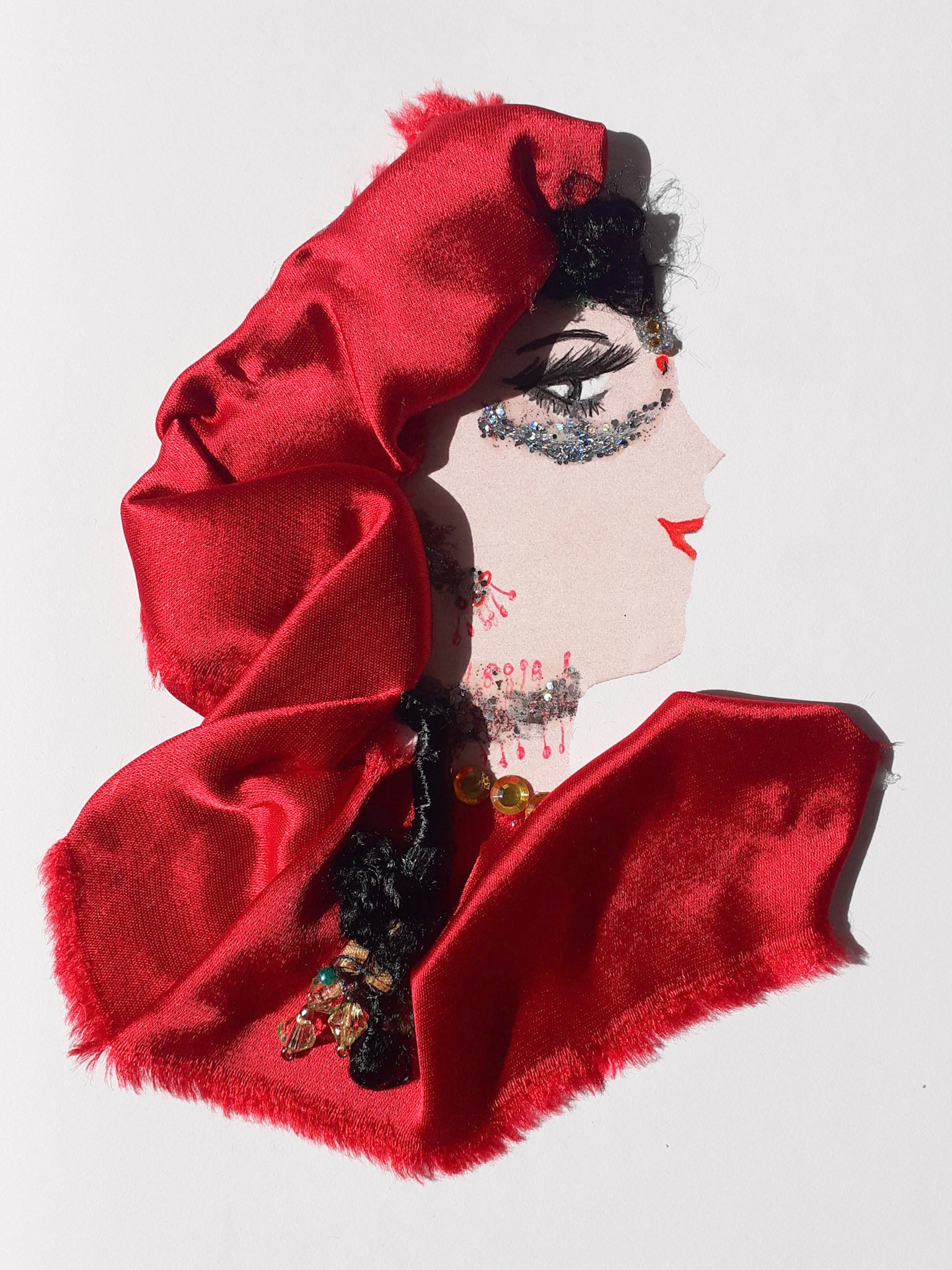 This card has been given the name Kelia. Kelia wears a red satin headscarf. Her black curly braid drapes down her side. She wears silver glittery face jewellery.