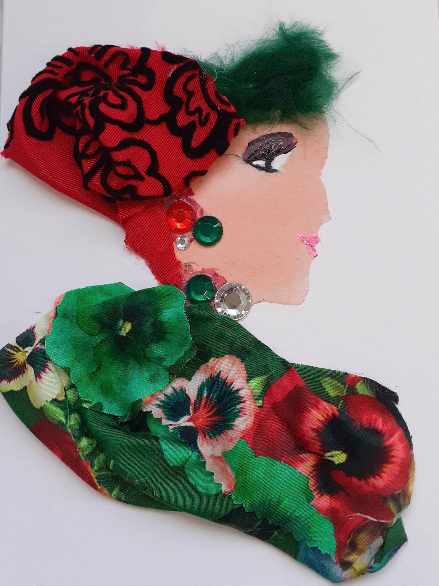 This card is given the name Claudia Cloverleaf. Claudia wears a floral print fabric with green and red flowers, and a red headdress to cover her green hair which has black embroidery on it.