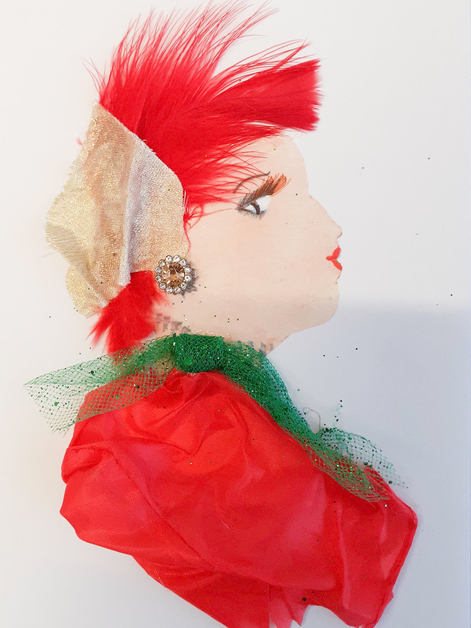 She wears a red silk dress with a green chiffon bow, and her hair is feathery and red with a gold silk scarf in it