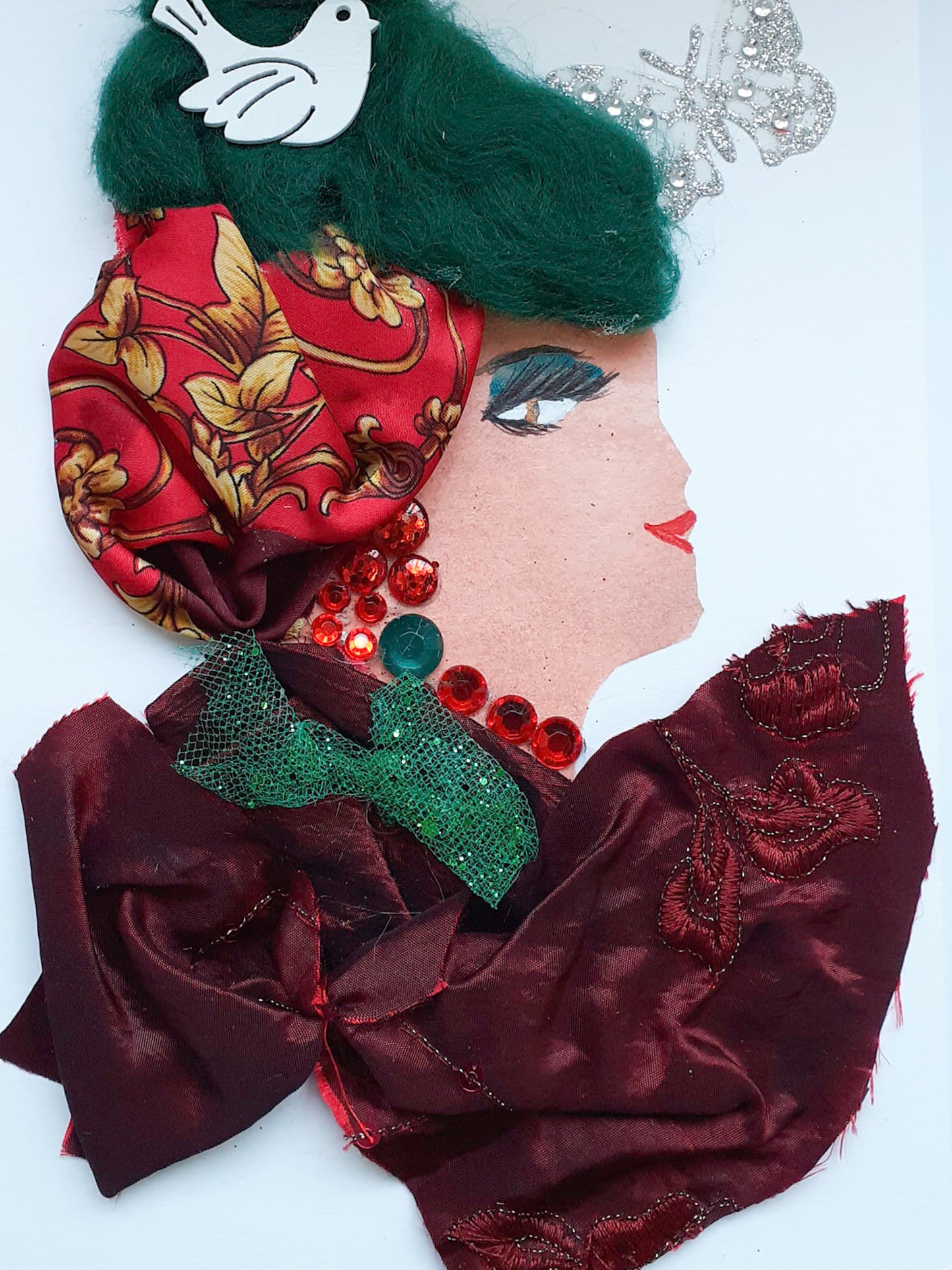 This card has been given the name Peaceful Paarish. She wears a dark red fabric blouse with a small green mesh bow, and a patterned silk scarf in her wooly green hair. She has a white dove in her hair, and a silver glittery butterfly next to her.