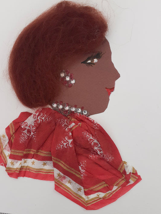 This card has been given the name Jollof Jenny. She wears a festive blouse that is red and has snowflakes on it. Her hair is short and brown with a tint of red.