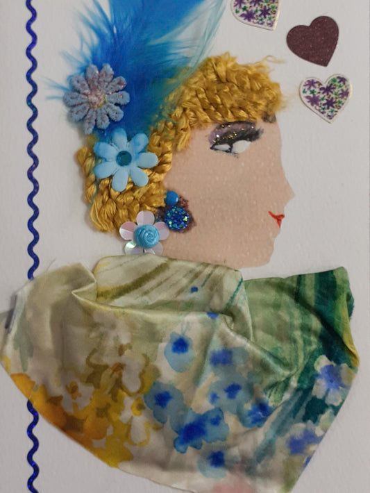 Leyton Lisa is wearing a multi- pastel printed blouse coloured dress with turquoise feathers on her hair attached with two flowers. There are three hearts on the right side with a blue squiggle line going down the card on the left.